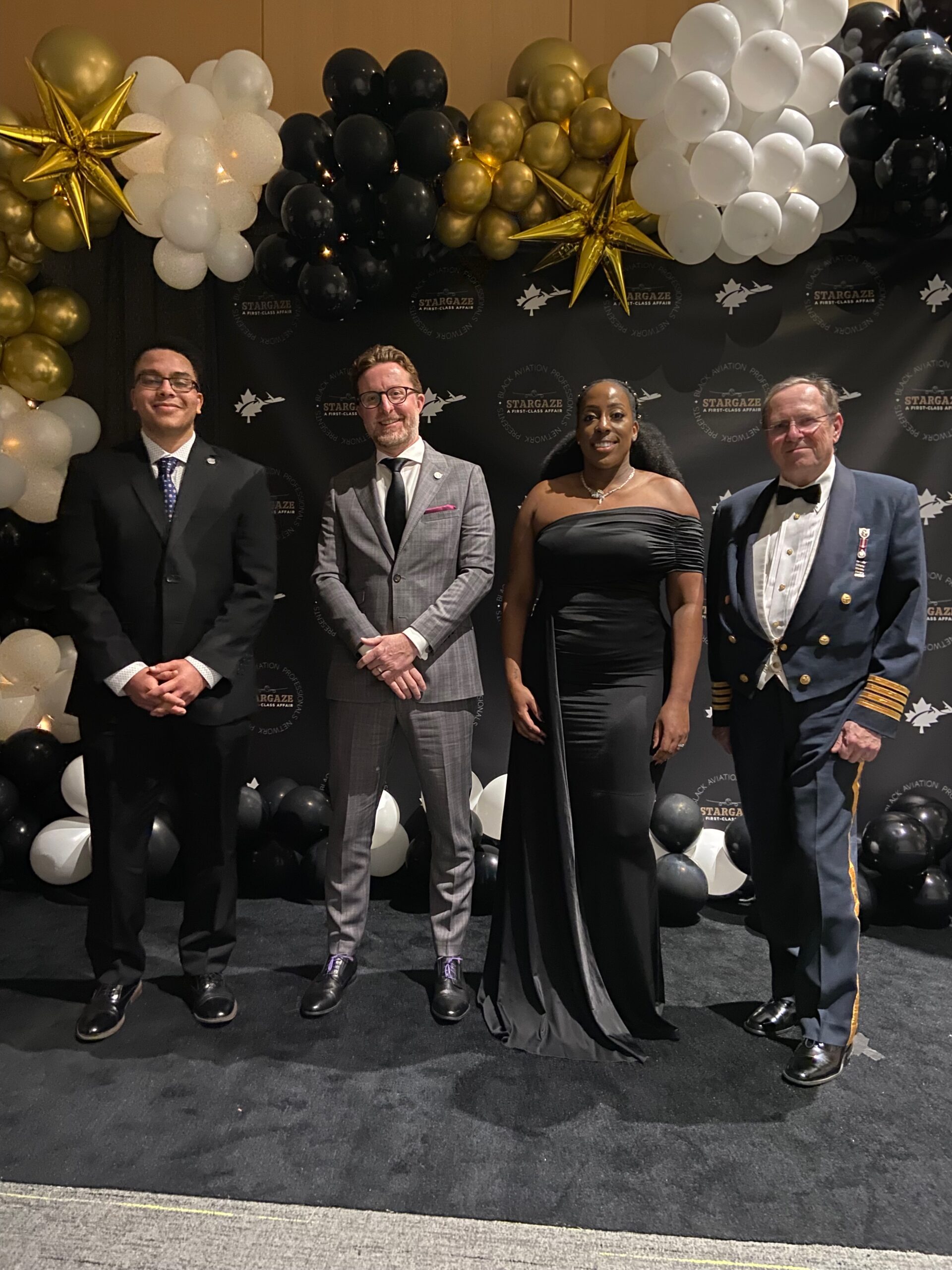 Photo of Adam Gibson, Jeremy Diamond, John Wright, and Tonya Yearwood posing on gala backdrop with balloons.
